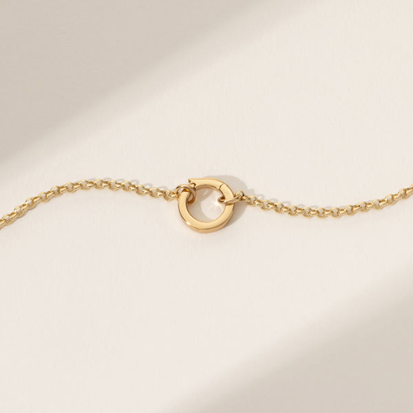 A gold chain bracelet with a gold latch ring in the center, set against a white background with light shadows.