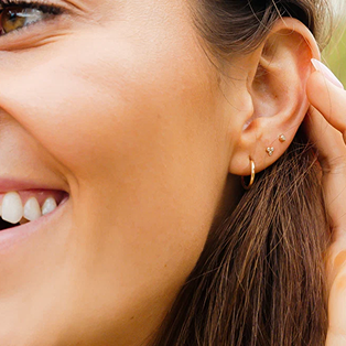 A person's ear wearing a gold hoop earring and two small gold studs.