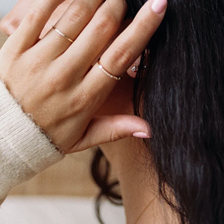 A person's hand wearing two dainty gold rings with small clear diamond stones.