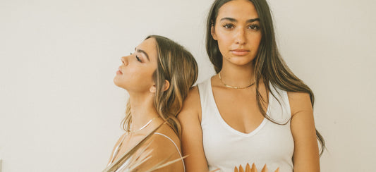 Two girls standing in front of a solid light beige surface.