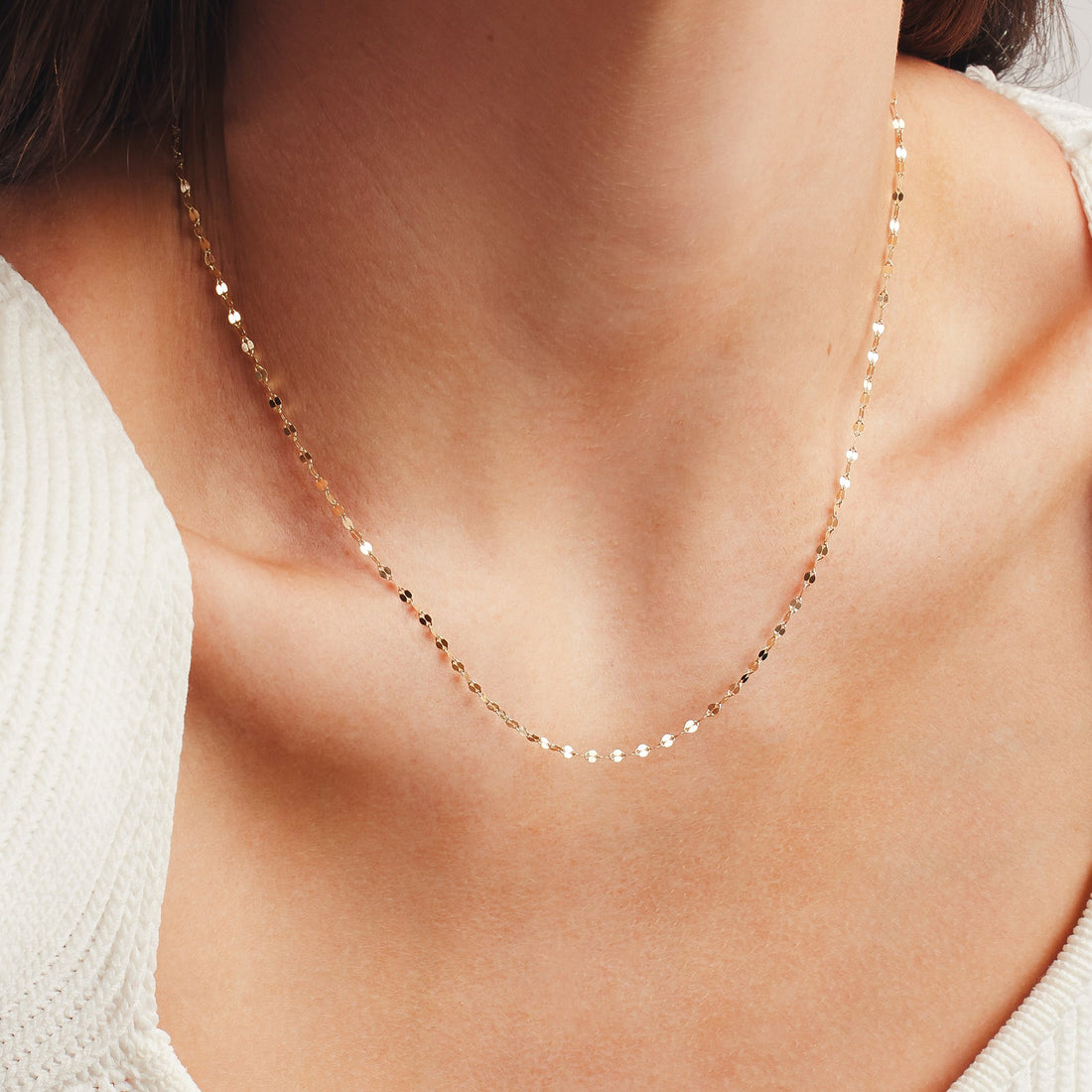 A woman wearing a delicate textured gold chain necklace.