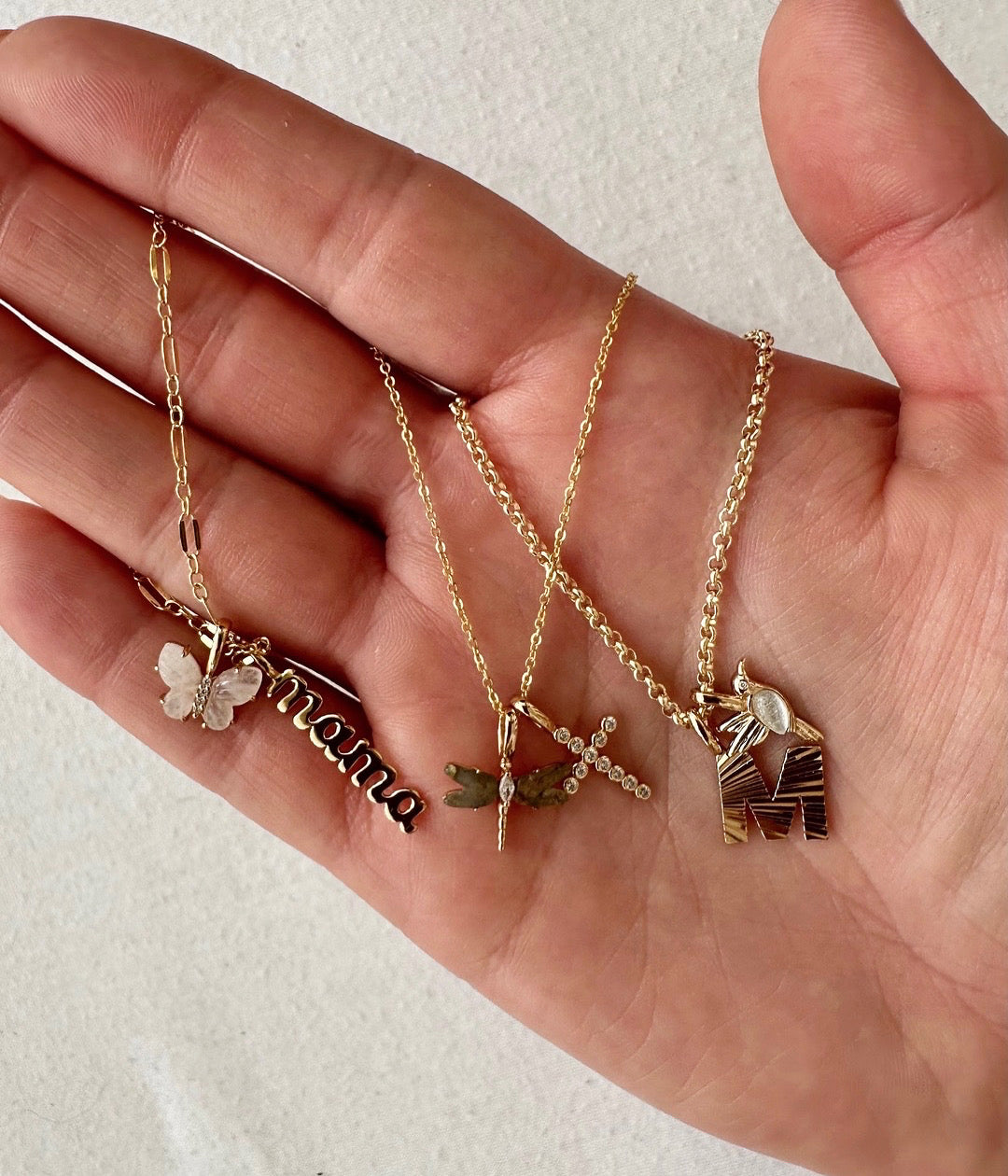 A person's hand holding multiple gold chain necklaces with charms.