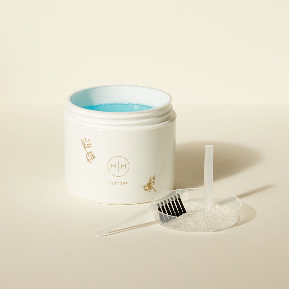 A white tub of blue jewelry cleaning liquid with a brush, shown on a solid light beige surface.