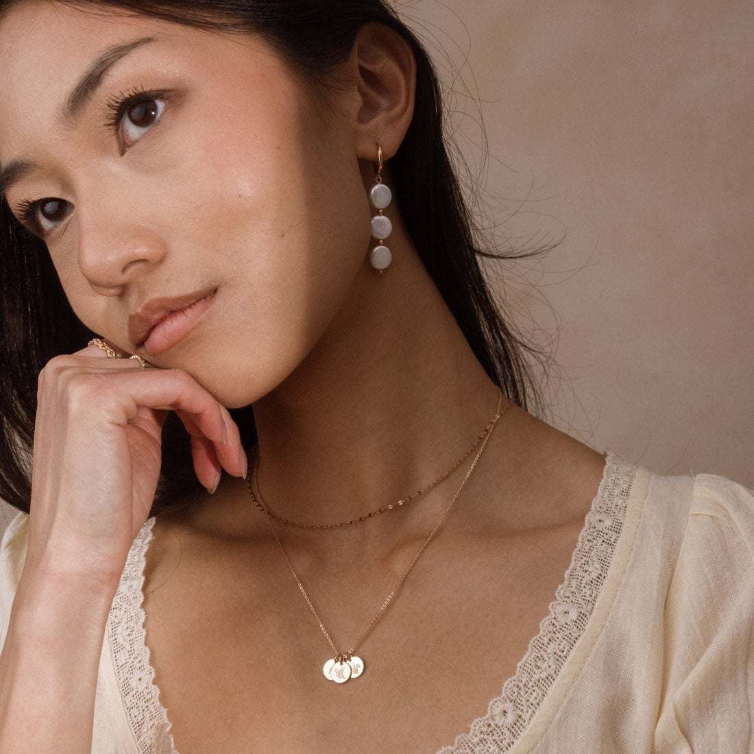 A model wearing gold stacker necklaces layered at the collarbone.