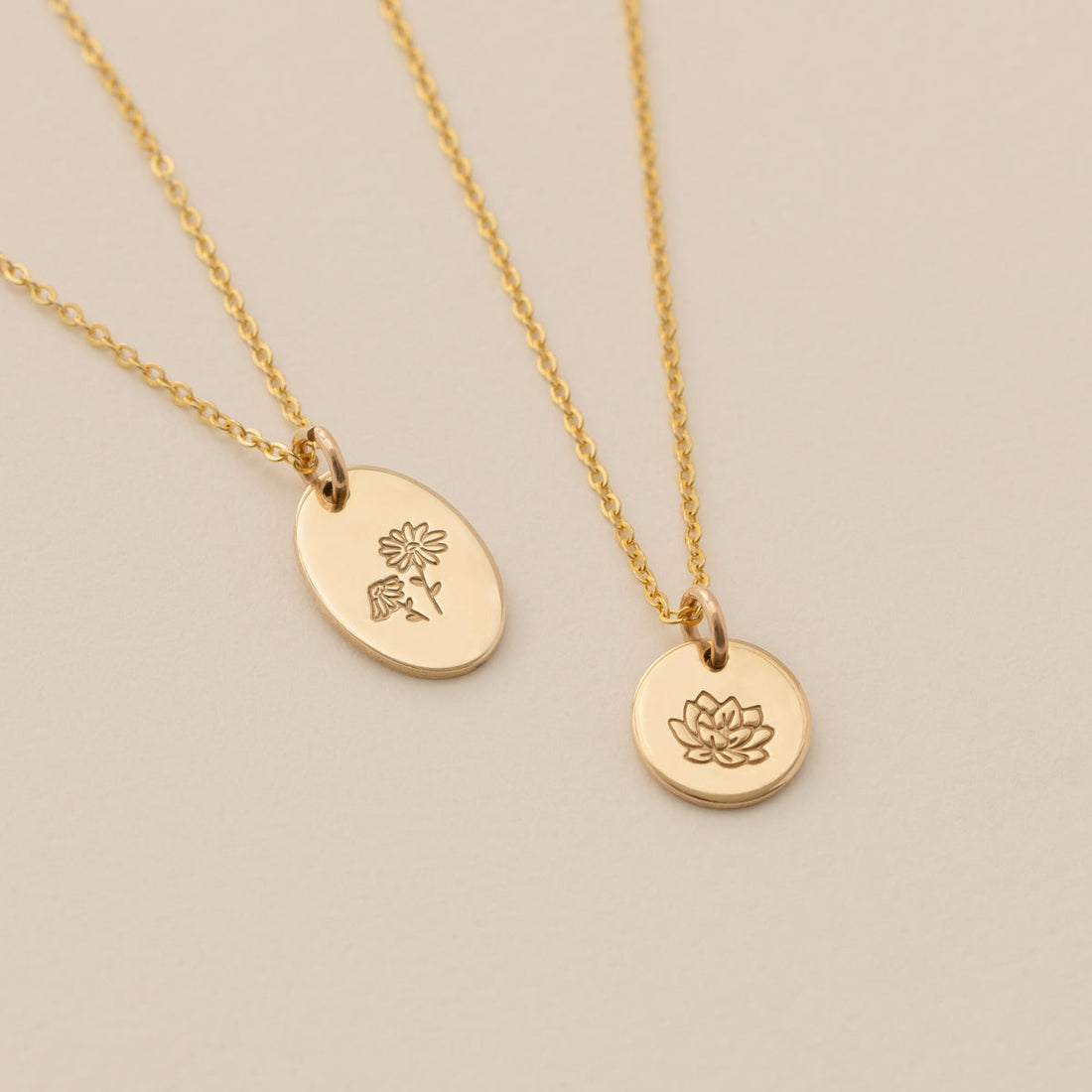 Two gold pendant necklaces, one with a flat oval and one with a round disc charm, each engraved with floral designs.