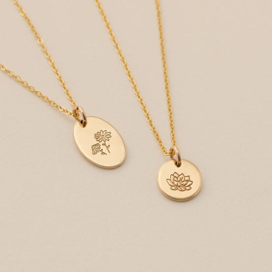 Two gold pendant necklaces, one with a flat oval and one with a round disc charm, each engraved with floral designs.