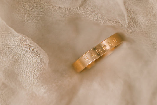 A gold engraved ring with the word 'HARPER' on a light beige surface.