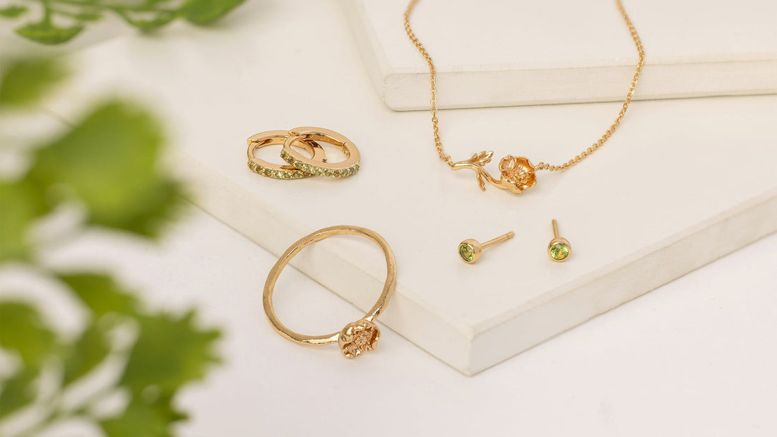 A flatlay of gold jewelry featuring a poppy flower and light green gemstones.