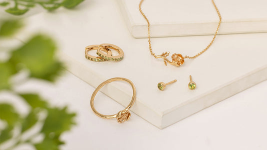 A flatlay of gold jewelry featuring a poppy flower and light green gemstones.
