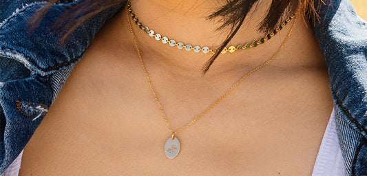 A woman wearing a poppy choker necklace layered with a gold pendant chain and engraved oval charm.