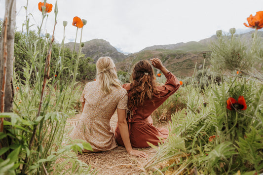 Two women sitting on a trail in a meadow surrounded by greenery.