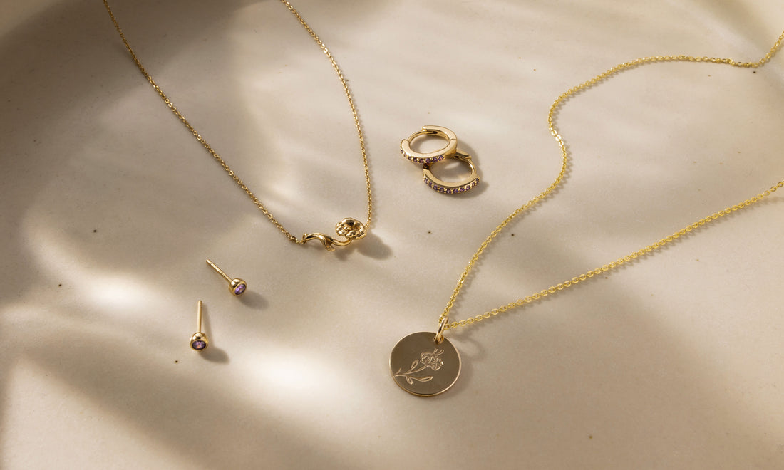Multiple pieces of gold jewelry with purple gemstones and violet flowers symbolizing February.