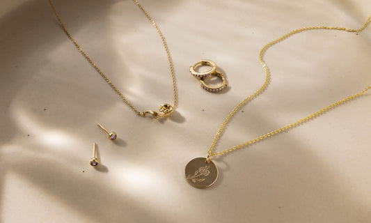 Multiple pieces of gold jewelry with purple gemstones and violet flowers symbolizing February.