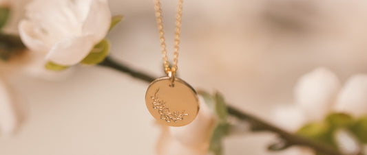 A gold round disc pendant necklace with a cherry blossom engraving