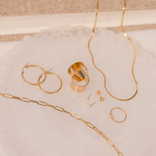 Multiple piece of gold minimalistic jewelry laying on a white stone surface.