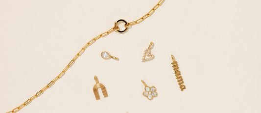A gold charm necklace laying beside multiple charms.