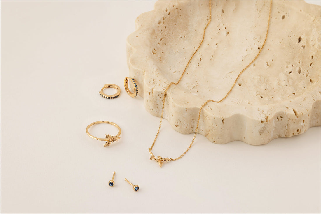Multiple pieces of gold jewelry with blue gemstones and a holly flower to symbolize December.