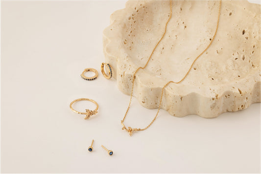 Multiple pieces of gold jewelry with blue gemstones and a holly flower to symbolize December.