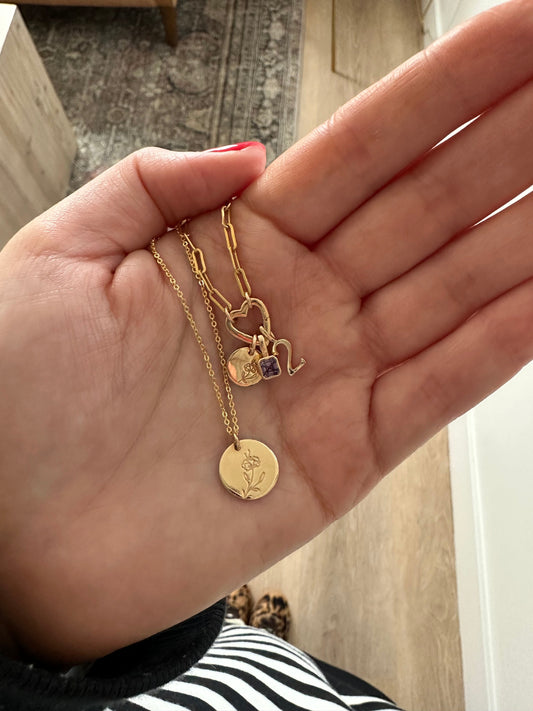 A hand holding a gold round disc pendant necklace and a gold charm necklace.