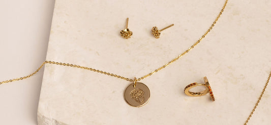 Multiple pieces of gold jewelry with carnation flowers and red gemstones symbolizing January.