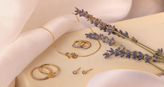 Multiple pieces of gold jewelry with rose flowers and light purple gemstones representing June.