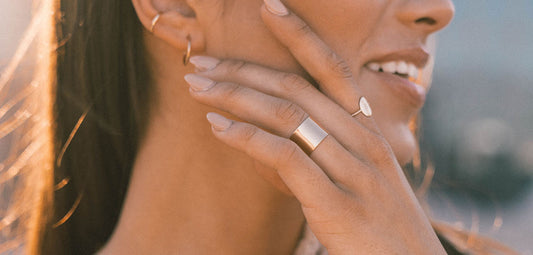 A woman with her hand resting on her face, wearing gold rings and gold earrings.