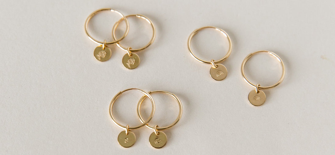 Three pairs of gold thin hoop earrings with small round discs hanging from them.