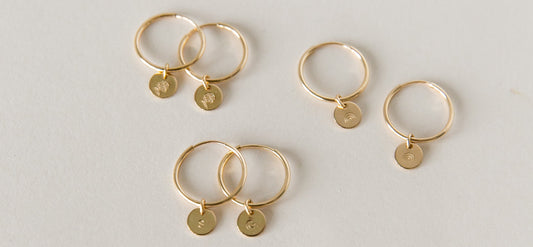 Three pairs of gold thin hoop earrings with small round discs hanging from them.