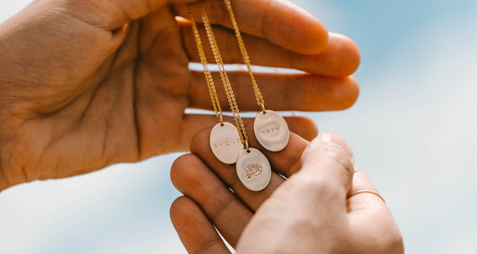A hand holding three gold oval pendant necklaces, each with a different engraving.