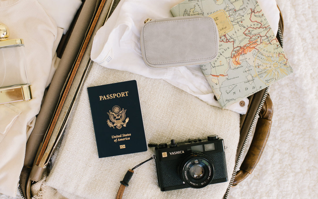 A suitcase filled with clothing, a camera, a passport, and a jewelry case.