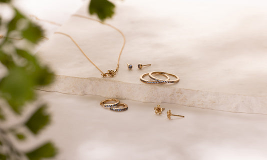 Multiple pieces of gold jewelry with light blue gemstones and cherry blossom flowers representing March