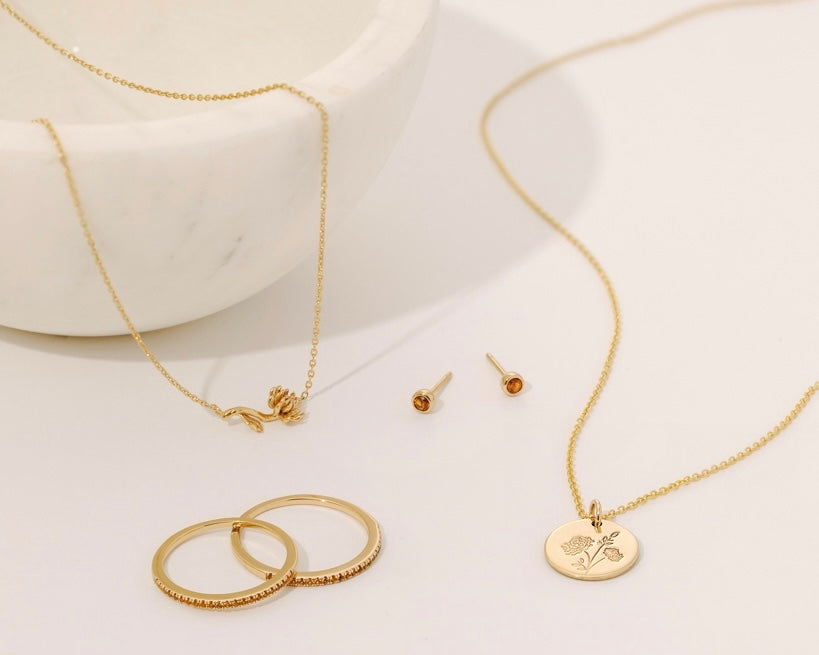 Multiple pieces of gold jewelry, each with either an amber birthstone or a chrysanthemum flower design representing November.