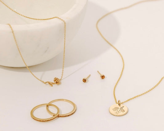 Multiple pieces of gold jewelry, each with either an amber birthstone or a chrysanthemum flower design representing November.