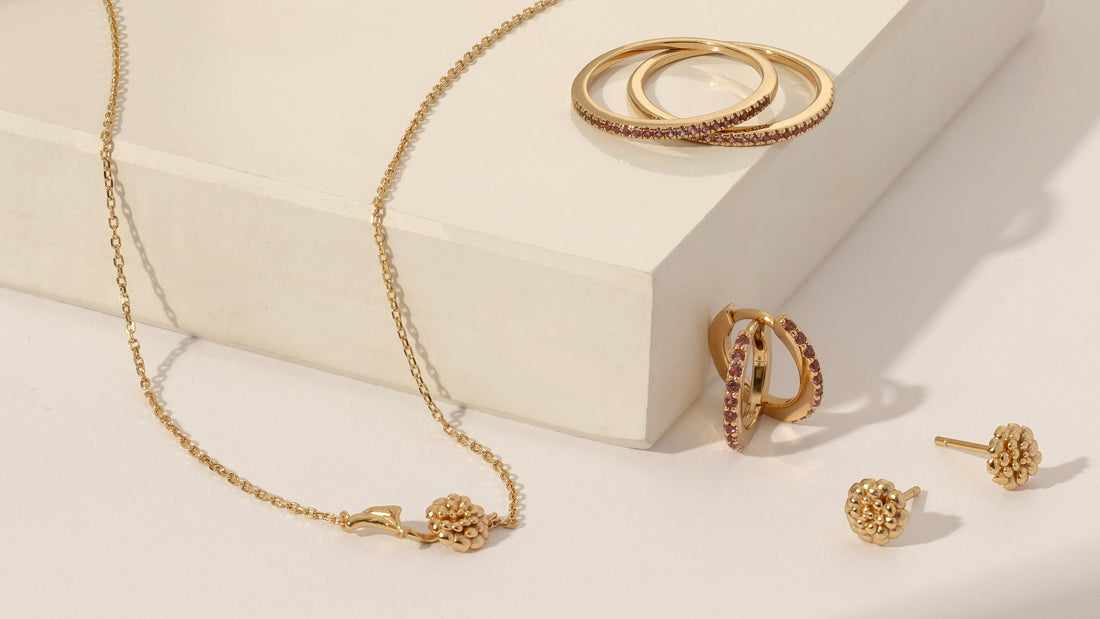 Multiple pieces of gold jewelry with pink gemstones and marigold flowers to symbolize October.