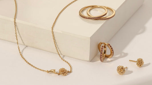 Multiple pieces of gold jewelry with pink gemstones and marigold flowers to symbolize October.