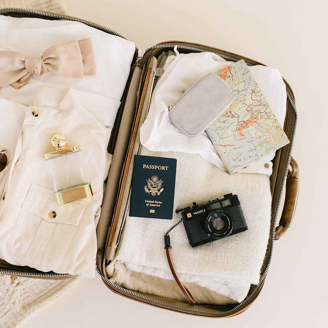 An open suitcase with clothing, a passport, and a jewelry case.