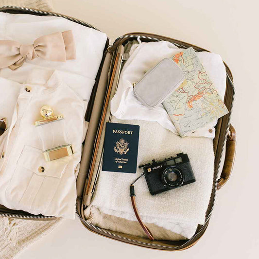 An open suitcase with clothing, a passport, and a jewelry case.