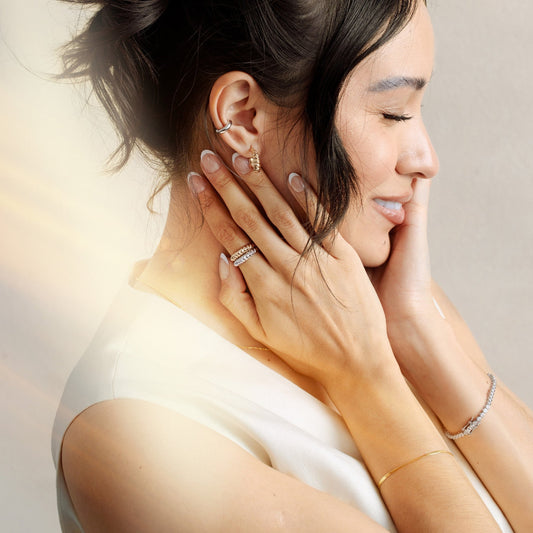 A woman with her hand resting on her neck, featuring two thick twisted rope rings in gold and silver.