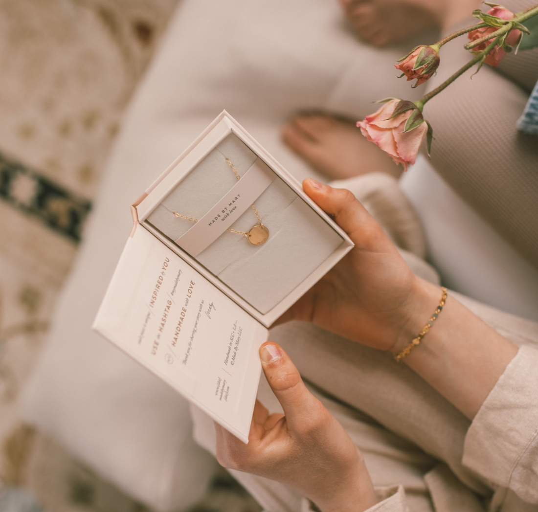 Hands holding an open jewelry box with a gold necklace inside.