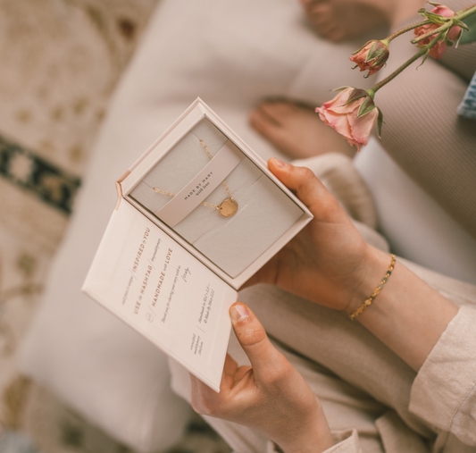 Hands holding an open jewelry box with a gold necklace inside.