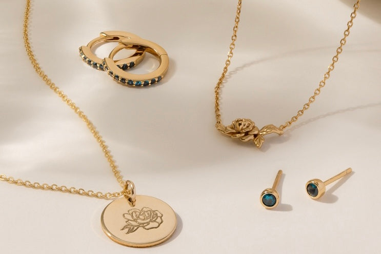 Multiple pieces of gold jewelry with blue-green gemstones and peony flowers representing September.