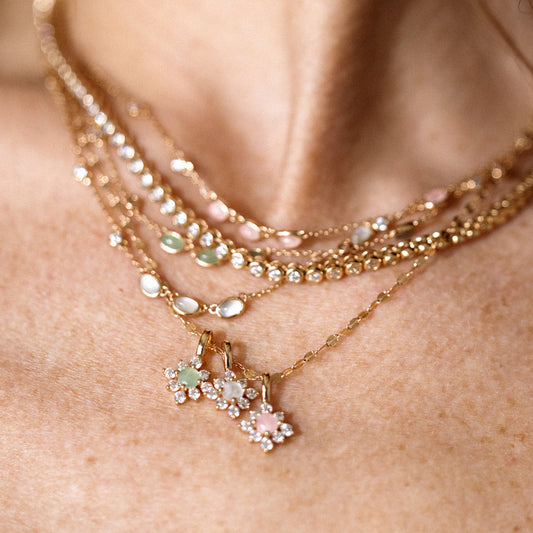 A model wearing multiple layered gold necklaces in different styles, including pendant necklaces with rose quartz, moonstone and green aventurine charms.