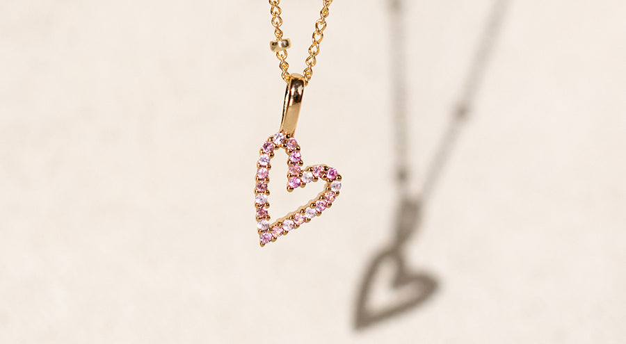 A heart charm with various pink colored stones on a delicate gold chain necklace.