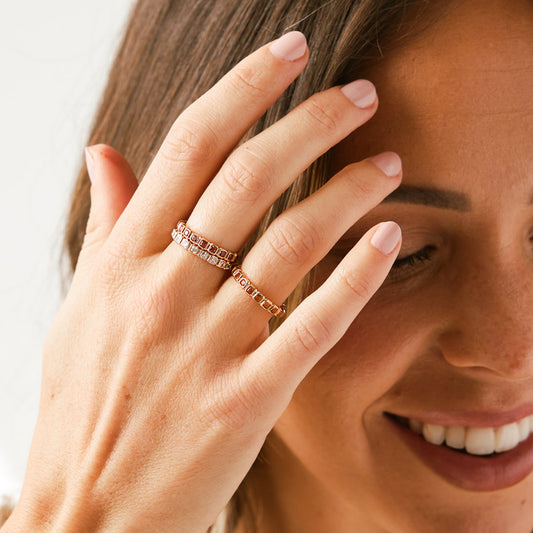 A woman wearing multiple gold eternity rings, each comprised of different color square gemstones.