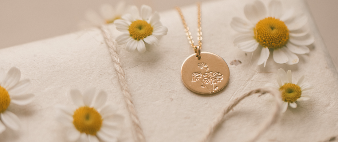 A gold round disc pendant necklace surrounded by white daisies.