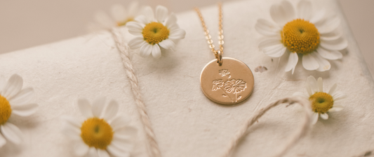 A gold round disc pendant necklace surrounded by white daisies.