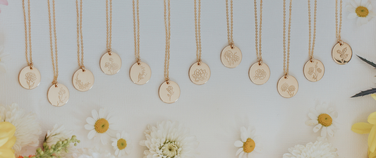 Twelve gold disc pendant necklaces hanging side by side, each engraved with a floral motif.