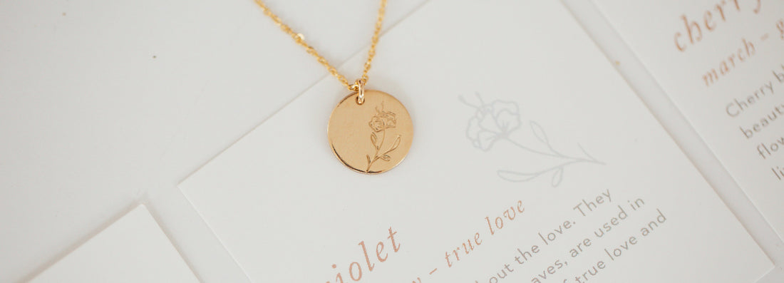 A gold round disc pendant necklace with a violet flower engraving.
