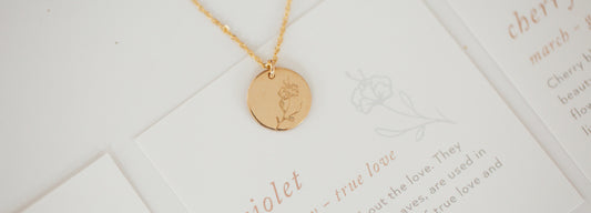 A gold round disc pendant necklace with a violet flower engraving.