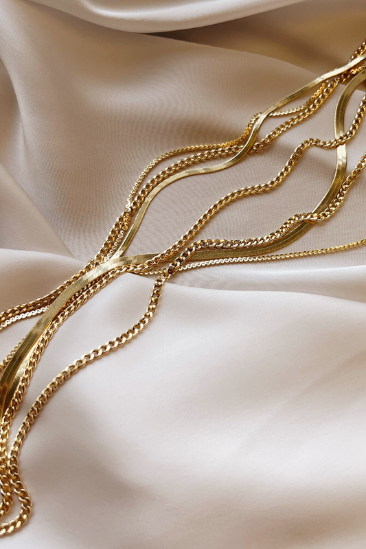 Gold chains draped on a light pink satin surface.